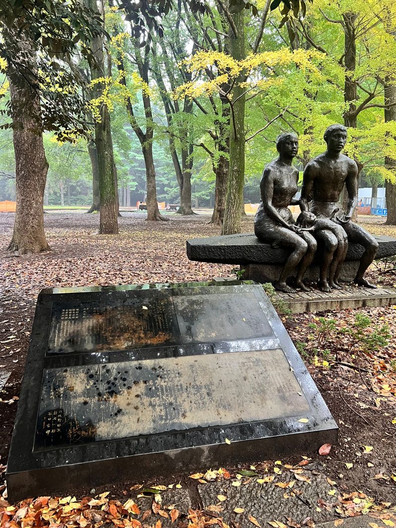 A bronze seated figure on a bench beside a peaceful park