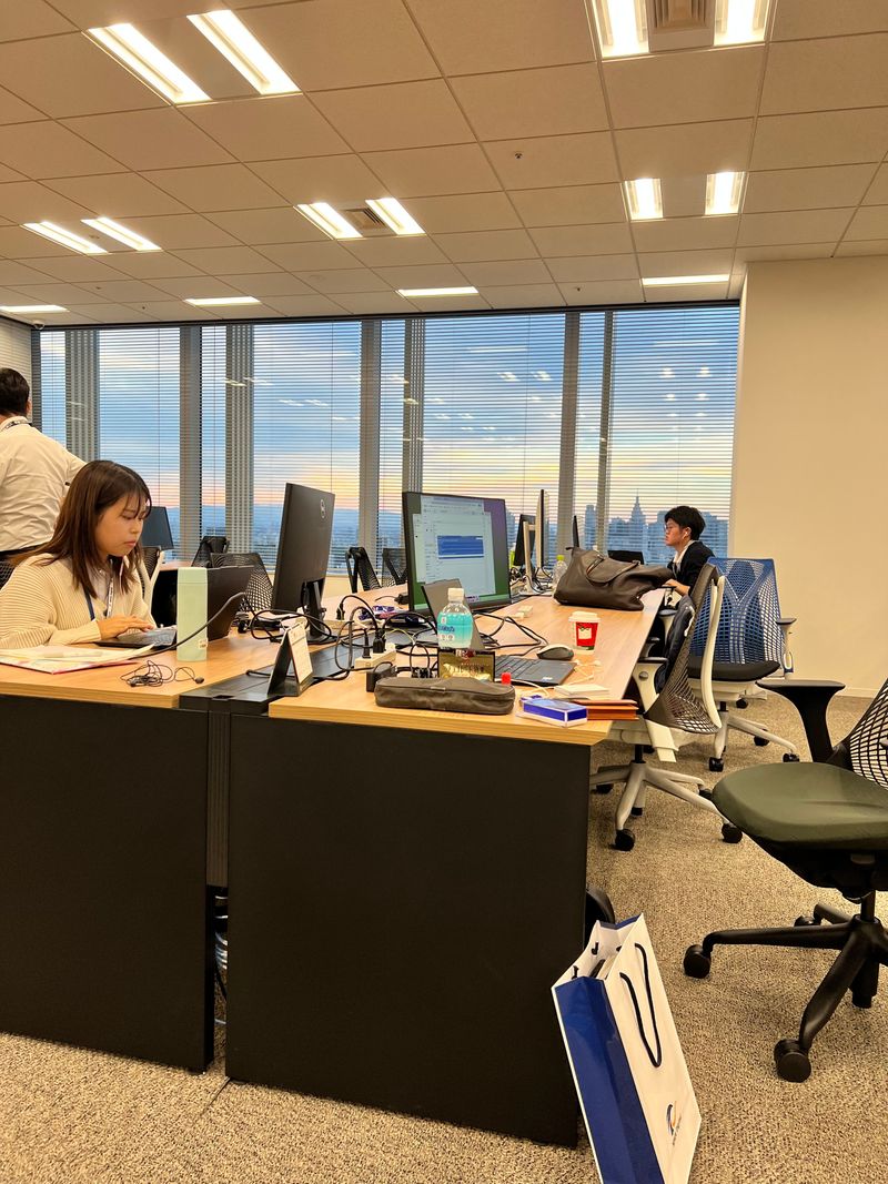 Colleagues working at desks beside a high-rise office window at dusk