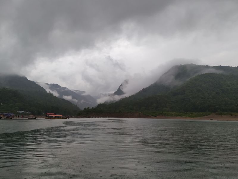 A misty lake surrounded by forested hills under heavy clouds