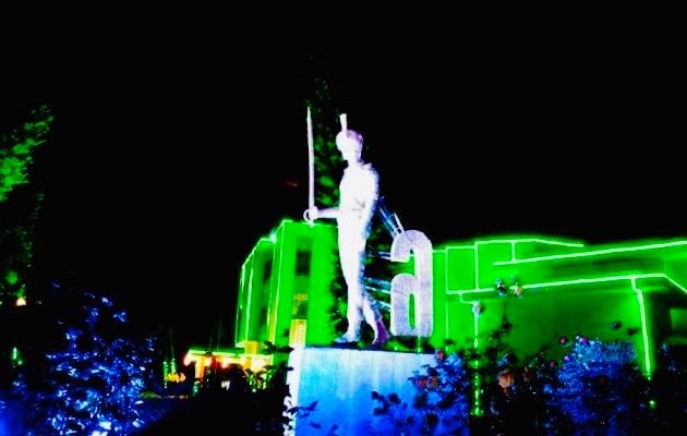 A statue of a cadet with sword lit green against a neon-outlined building at night