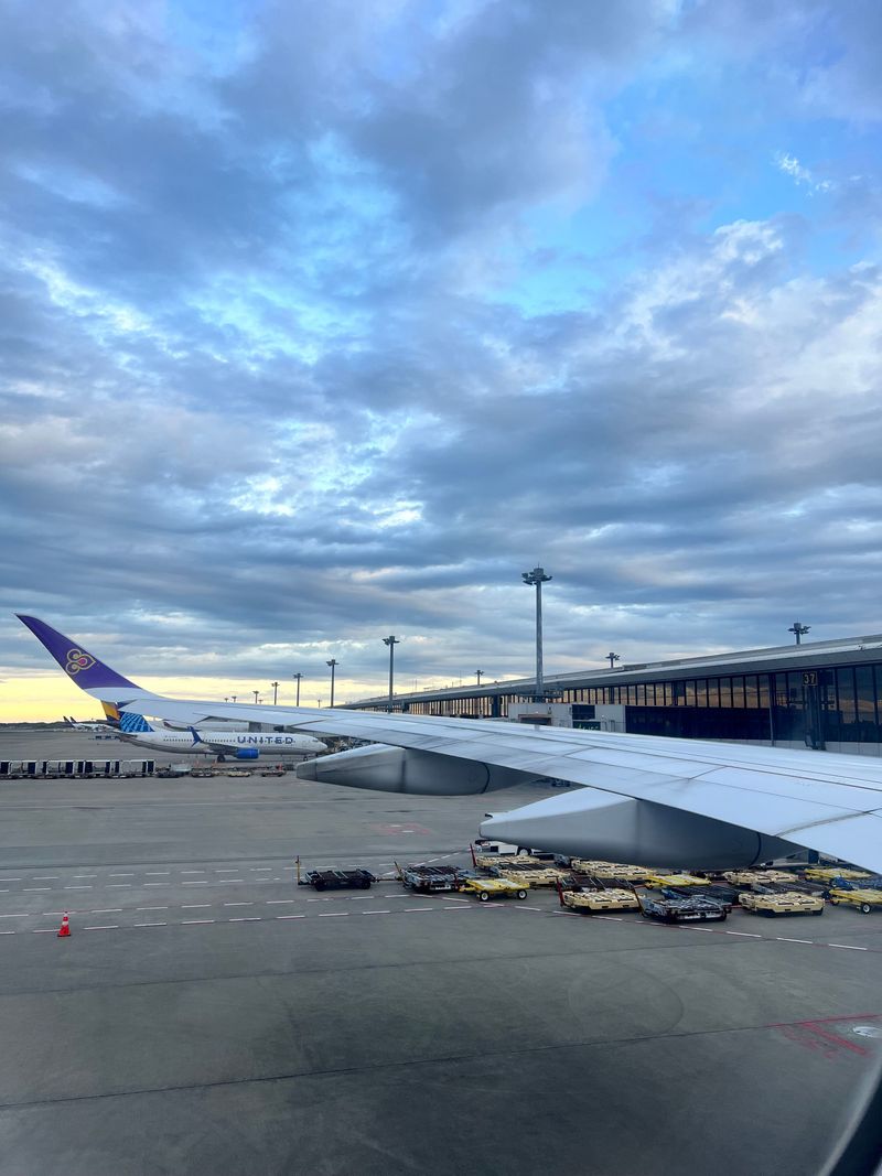 An airplane wing on the runway beneath a cloud-filled sky